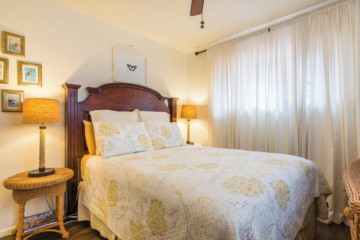 Una cama bien hecha con una colcha estampada floral, dos lámparas de noche y un cuadro en la pared.