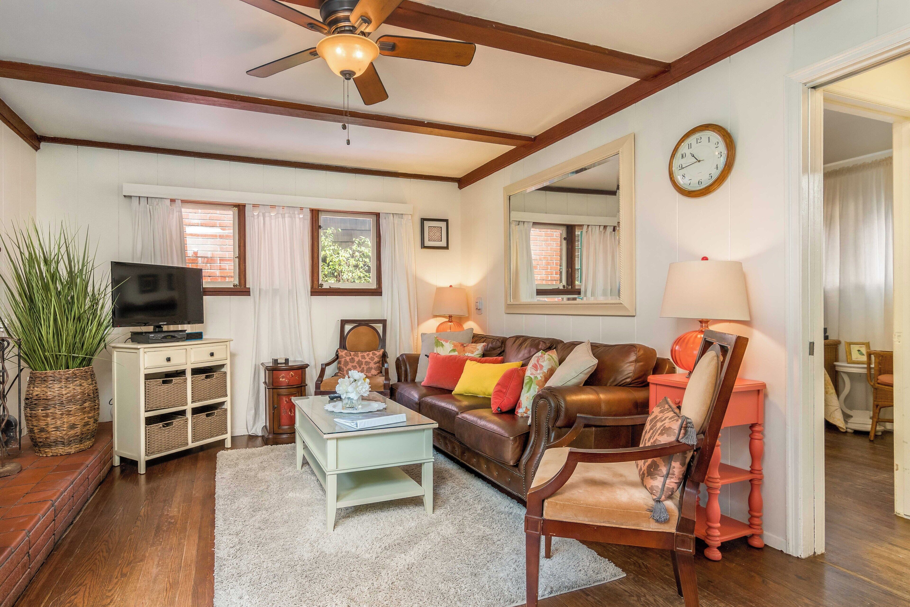 A living room with a television, a brown leather sofa, a white coffee table, and a ceiling fan.