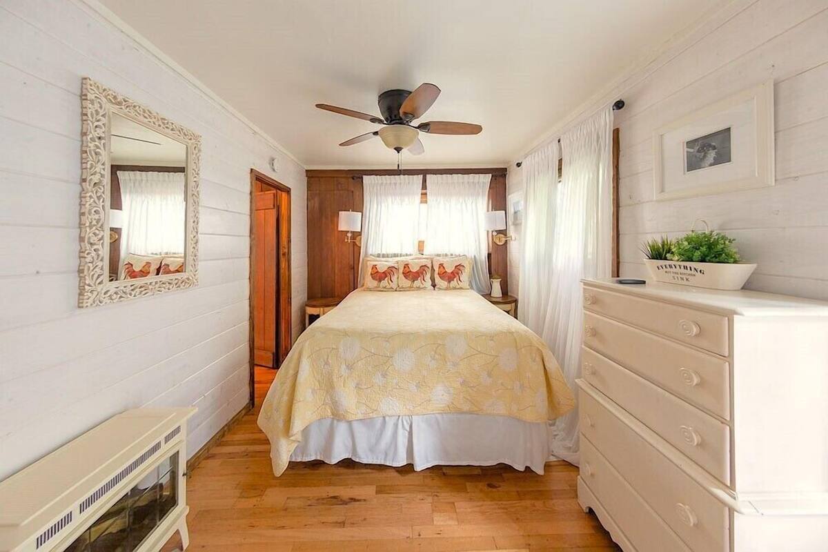 Un dormitorio con una cama, un ventilador de techo, un aparador y un espejo.
