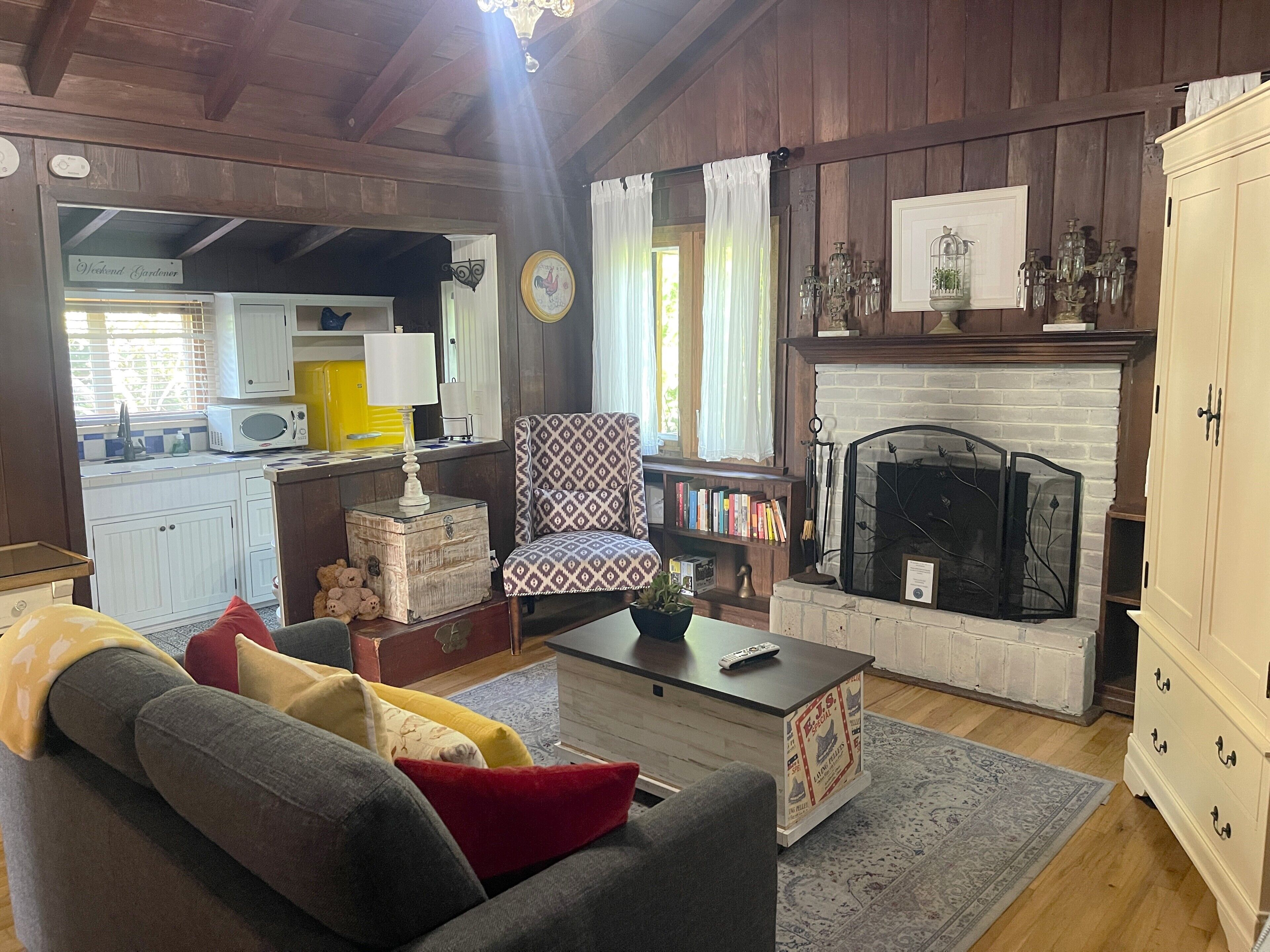 A cozy living room with a fireplace, a sofa with cushions, a coffee table, and a bookshelf.