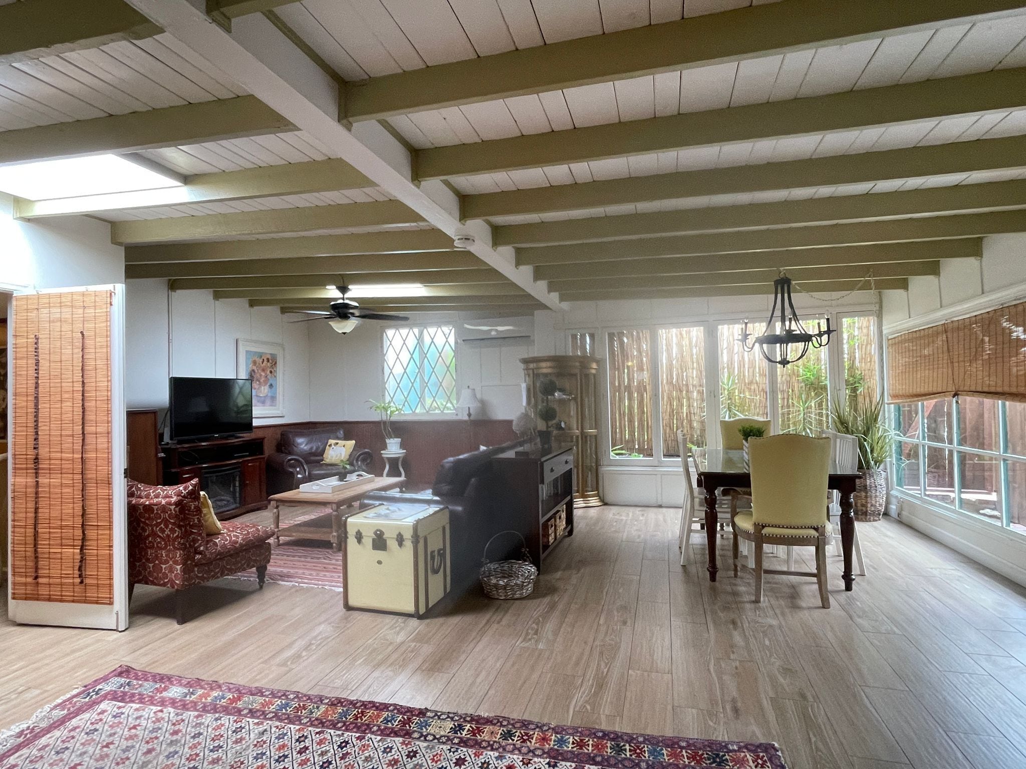 Un vaste salon doté d’un haut plafond, de poutres apparentes, d’un téléviseur, d’un canapé, d’une table basse et d’un coin repas avec une table et des chaises.