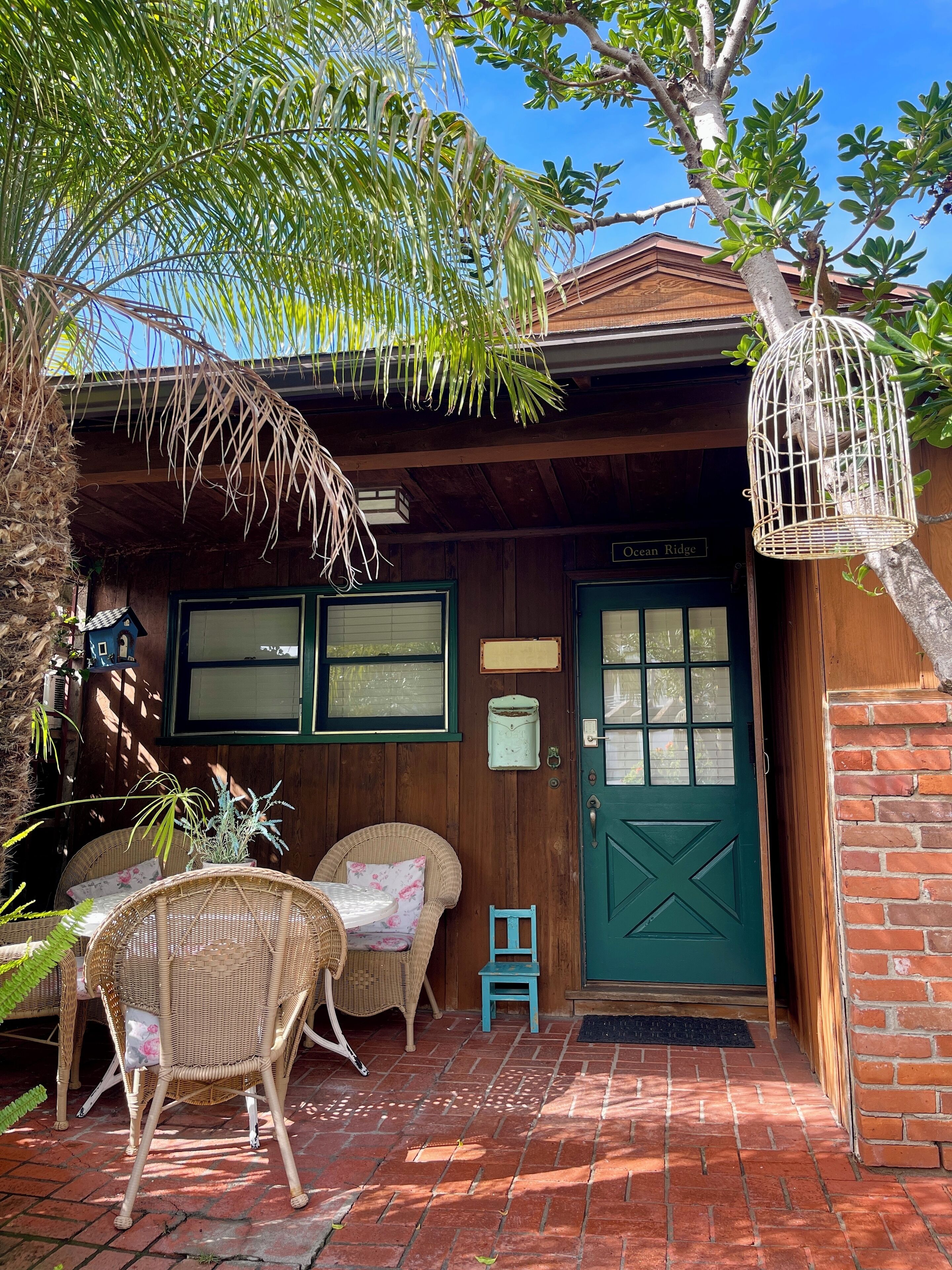 A wooden building with a green door, a small blue chair, wicker furniture, and a birdcage.