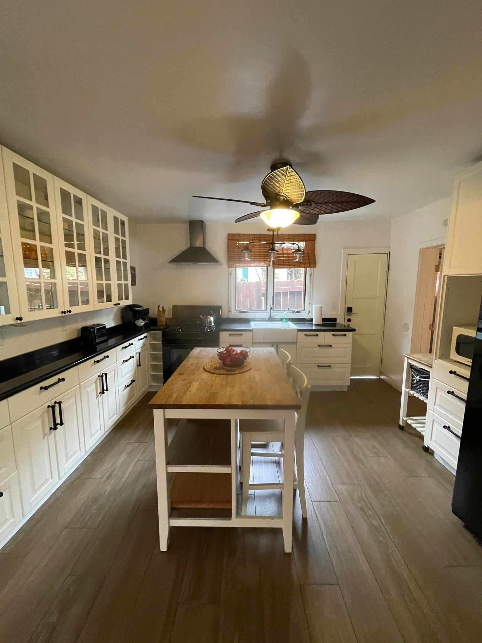 A kitchen with white cabinets, a wooden table, and a ceiling fan.