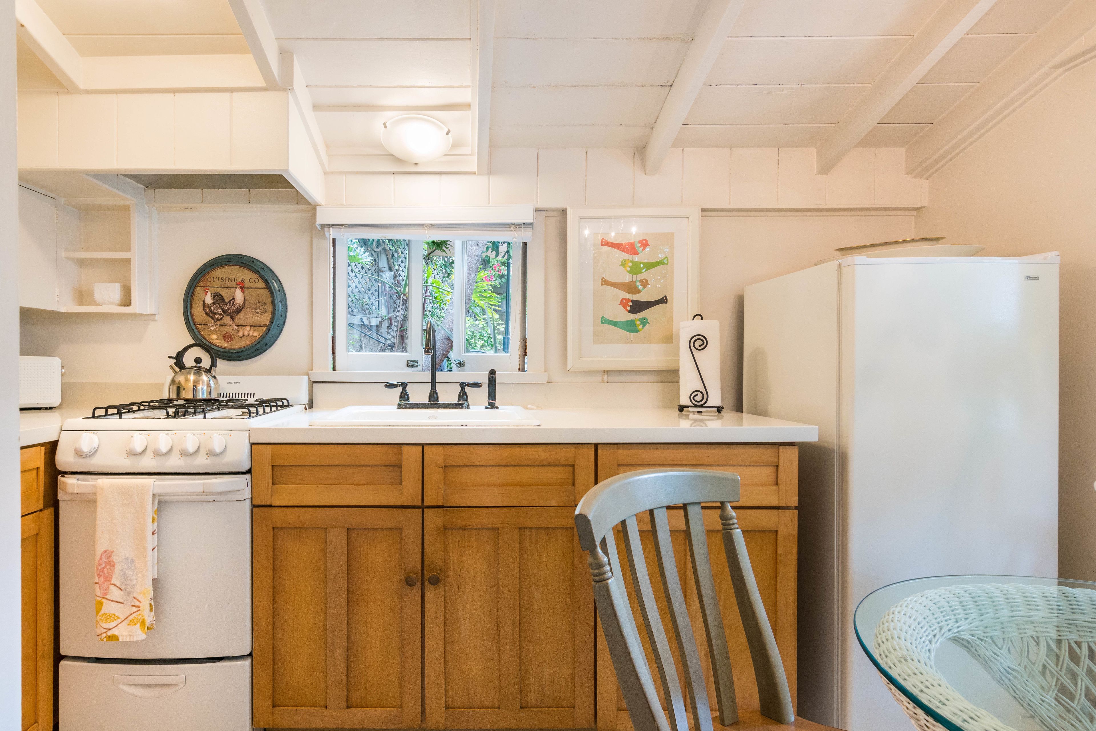 Una cocina con armarios de madera, una estufa a gas, un refrigerador y un ventanal con vista a la vegetación.