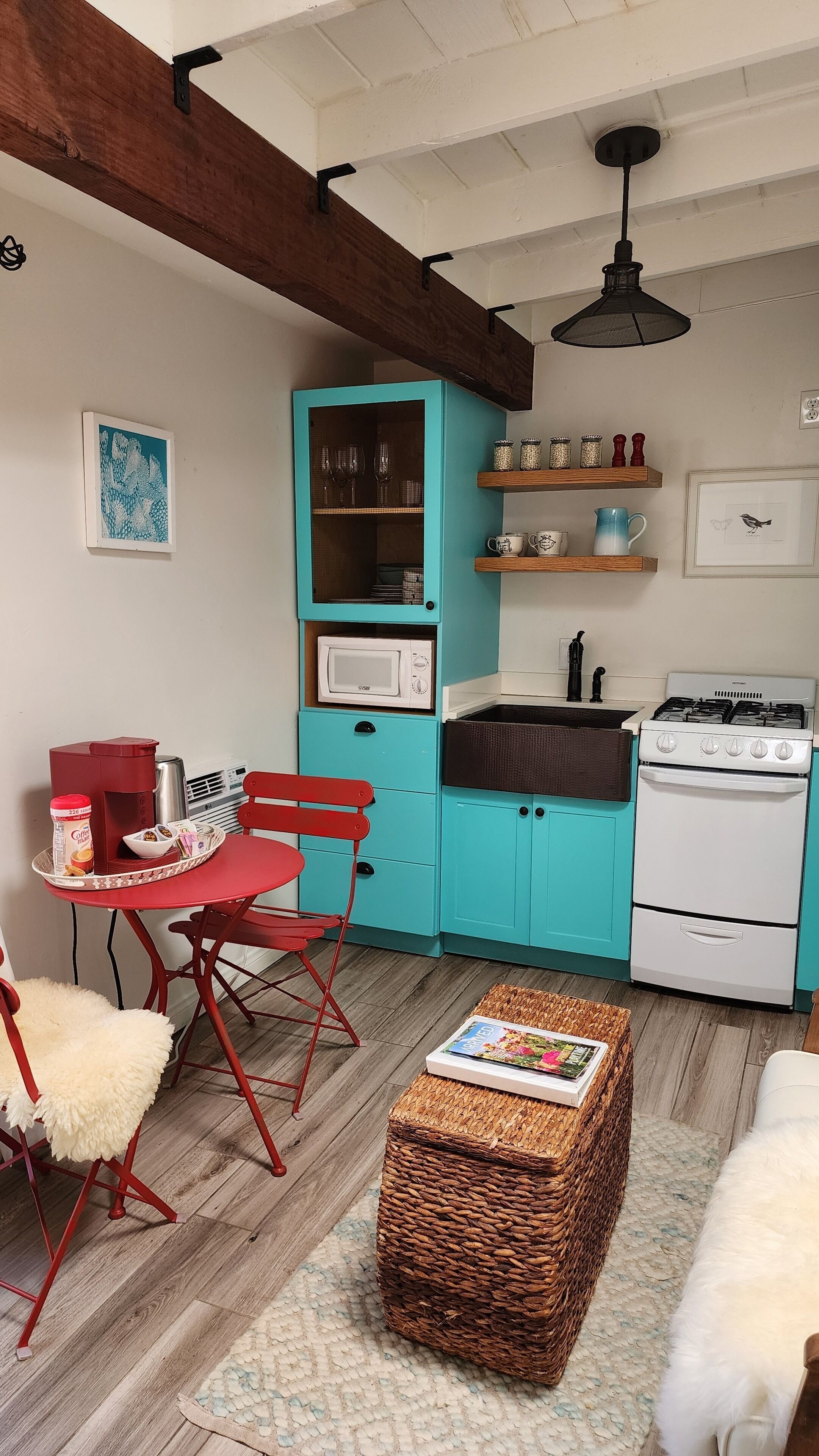 Una cocina compacta con gabinetes azul turquesa, una estufa blanca y una mesa de comedor roja con sillas.