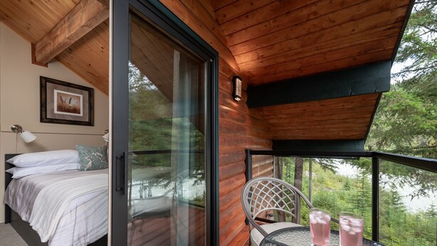 A bedroom with a bed, a nightstand, and a window overlooking a forest. - Mount Robson Mountain River Lodge (Mount Robson)
