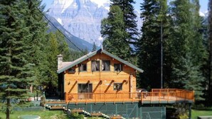 A wooden cabin with a balcony, surrounded by trees and a mountain in the background. - Mount Robson Mountain River Lodge (Mount Robson)