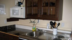 A kitchen with a stainless steel sink, a microwave, and a stove. There are cabinets above the sink and a glass cabinet above the stove. - Mount Robson Mountain River Lodge (Mount Robson)
