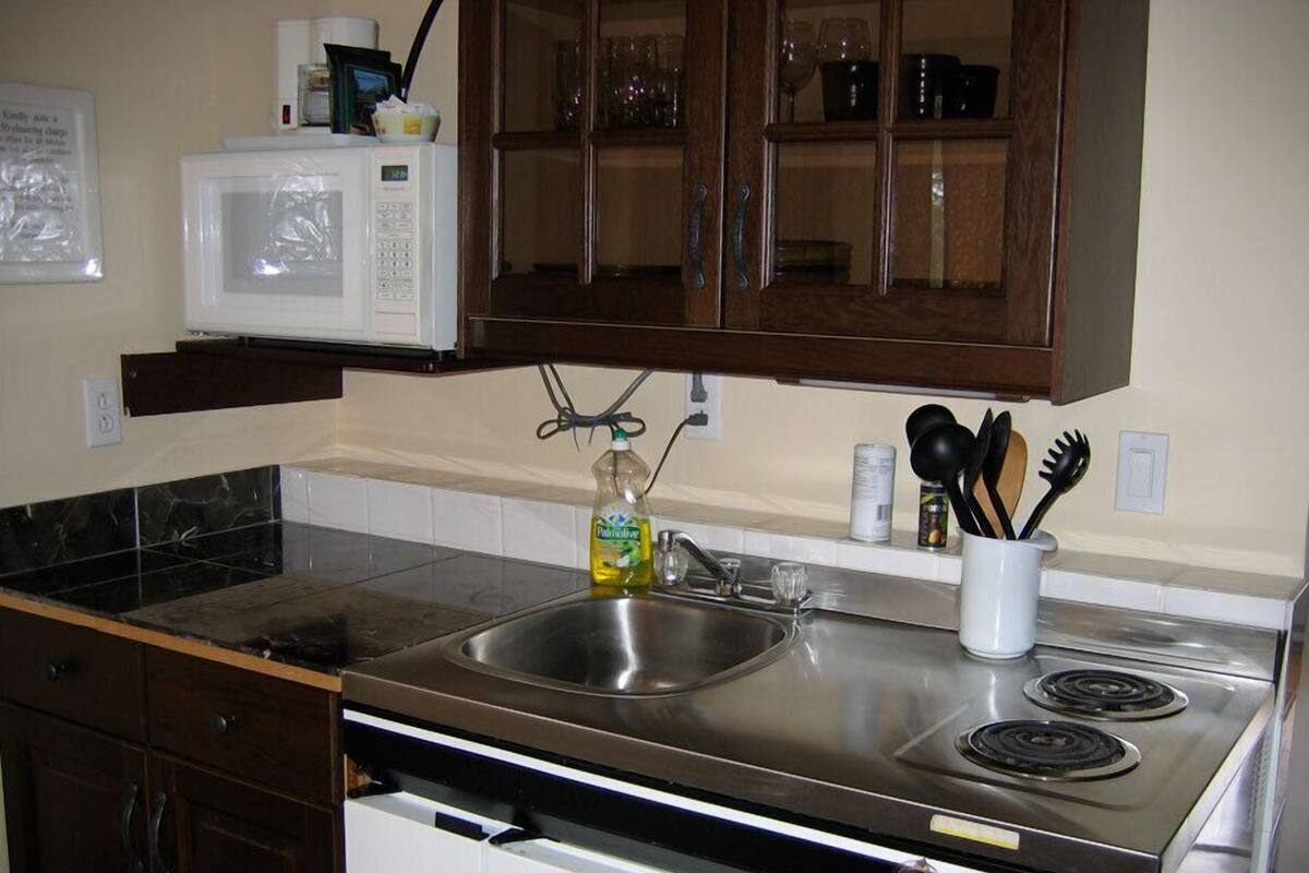A kitchen with a stainless steel sink, a microwave, and a stove. There are cabinets above the sink and a glass cabinet above the stove.