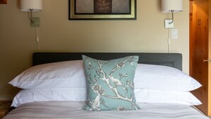 A neatly made bed with white linens and a single decorative pillow, a framed artwork above the bed, and two wall-mounted lamps on either side. - Mount Robson Mountain River Lodge (Mount Robson)