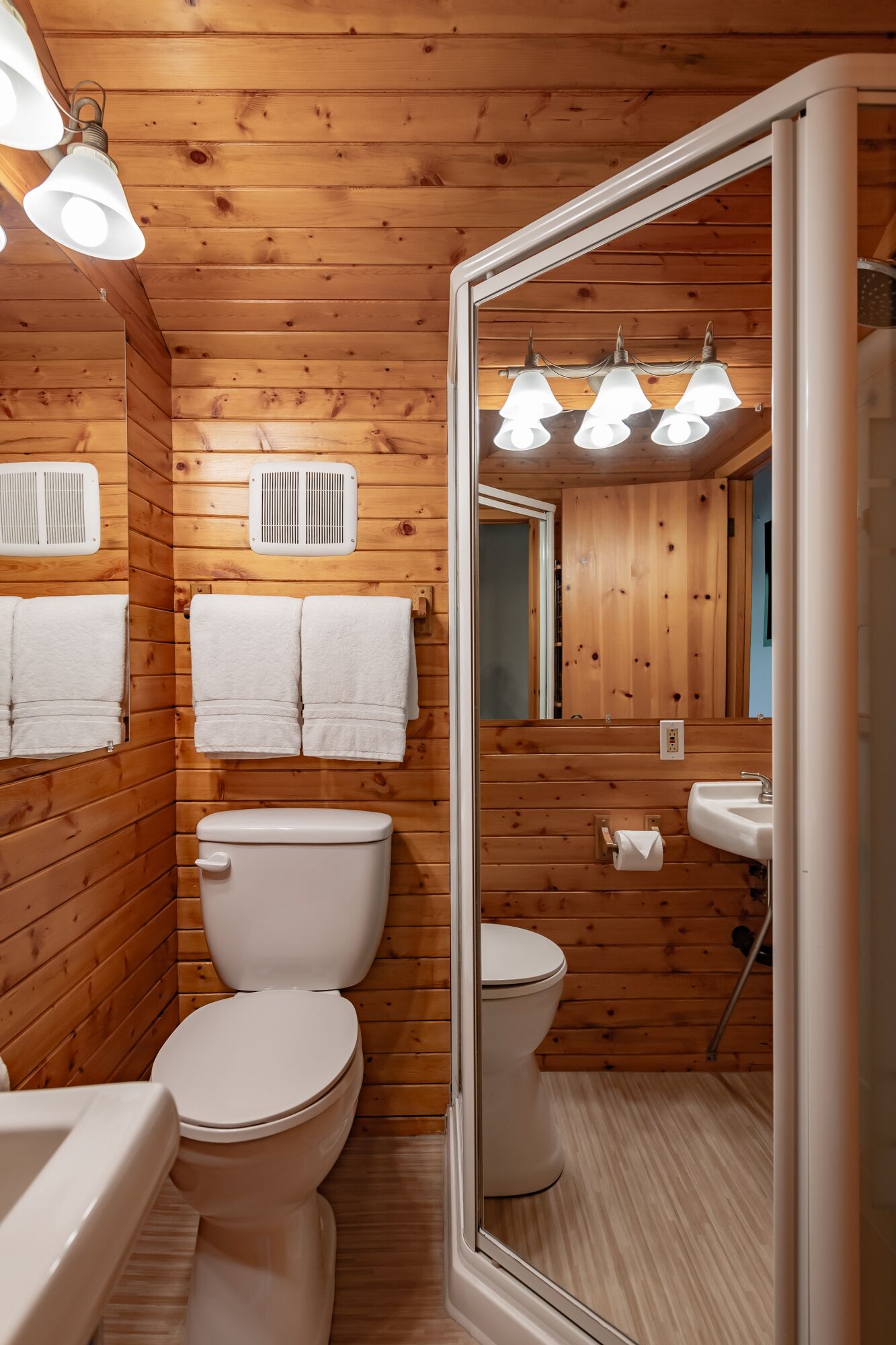 Un baño con paneles de madera, dos inodoros, un lavabo y un espejo.