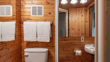 Un baño con paneles de madera, dos inodoros, un lavabo y un espejo.