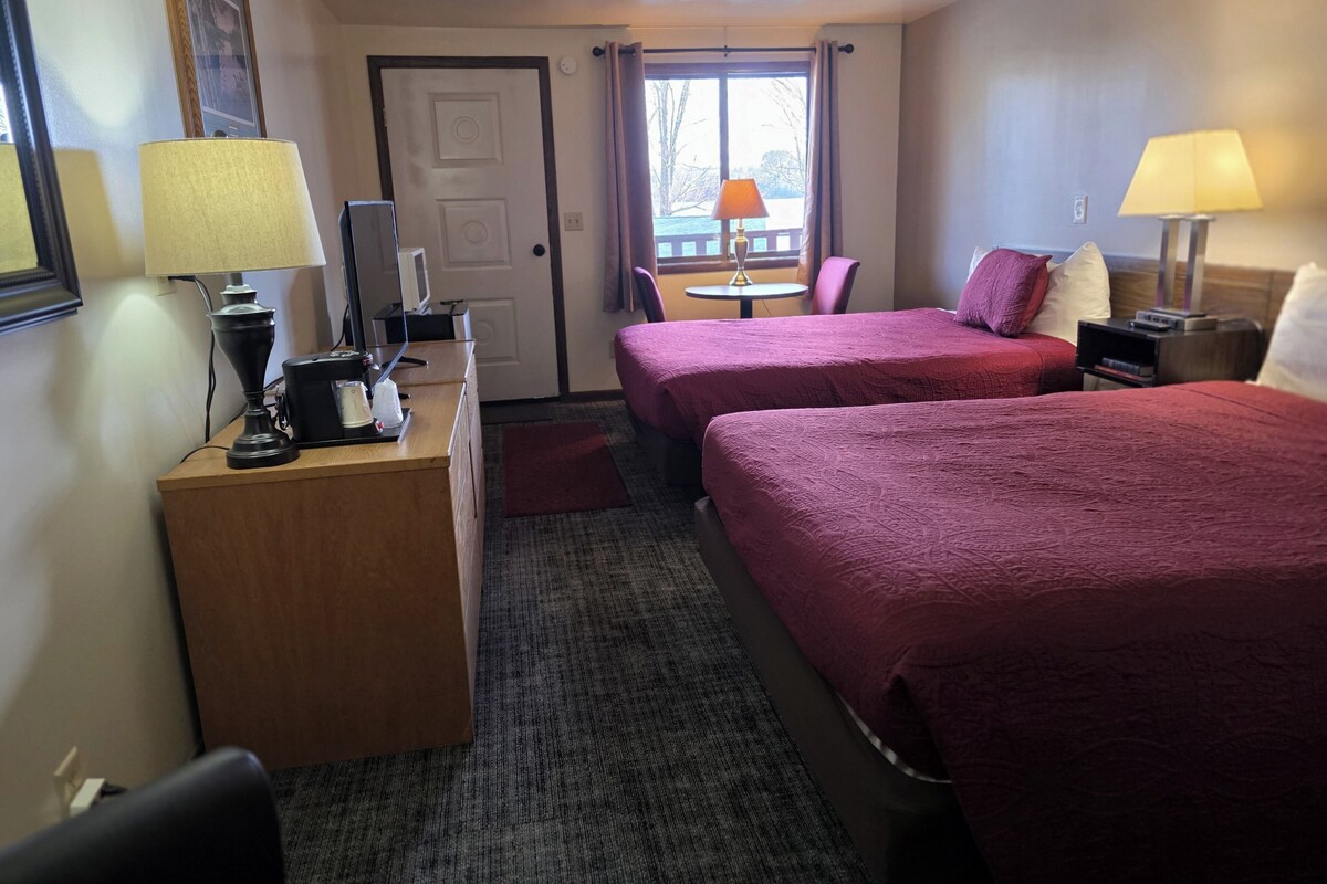Een hotelkamer met twee bedden, een bureau met lamp, een stoel en een kleine tafel met lamp.