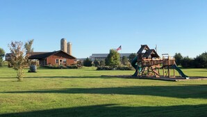 Un'area giochi con uno scivolo e strutture per arrampicarsi, una casetta di legno e silos in lontananza.