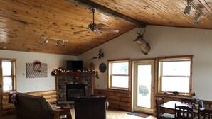 Interno di una baita in legno con camino, mobili in legno e una testa di cervo appesa al muro.