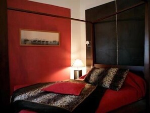 A bedroom with a red wall, a bed with a leopard print cover, and a painting above the bed. - Villa Blanche (Marseille)