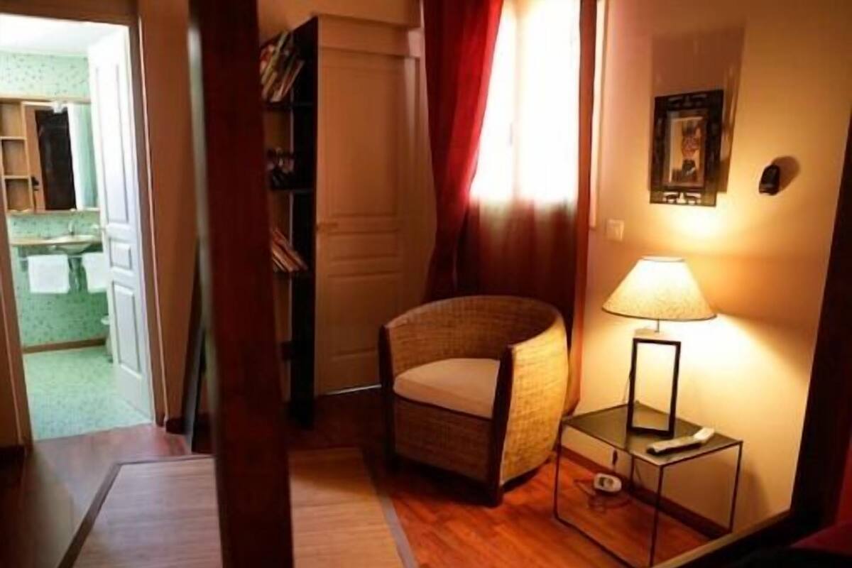 A cozy room with a wicker chair, a bedside table with a lamp, and a framed picture on the wall.