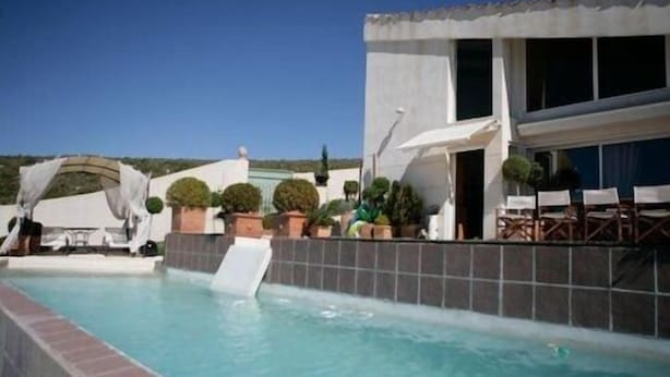 Une piscine avec un toboggan, entourée de plantes en pot et bordée d’un bâtiment dont la façade est recouverte de carreaux.