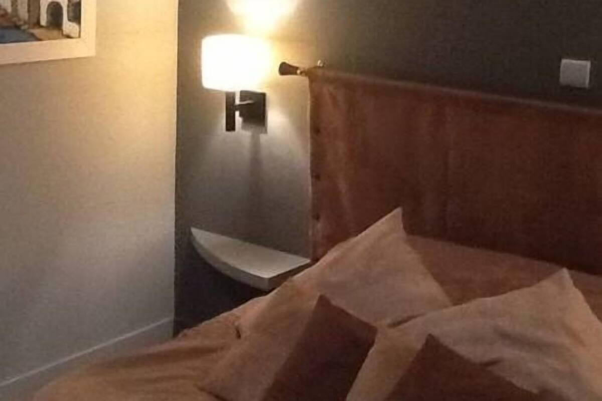 A bedroom with a bed, pillows, a nightstand, and a wall-mounted lamp.