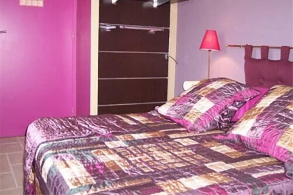 A bedroom with a bed, a pink wall, and a red lamp.