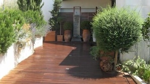 Une terrasse en bois mène à un bâtiment à l’extérieur blanc, doté d’un portail en métal.