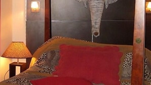 Une pièce dont le mur est orné d’une grande œuvre d’art représentant une tête d’éléphant, avec un lit doté d’un oreiller rouge et une lampe posée sur une table d’appoint.