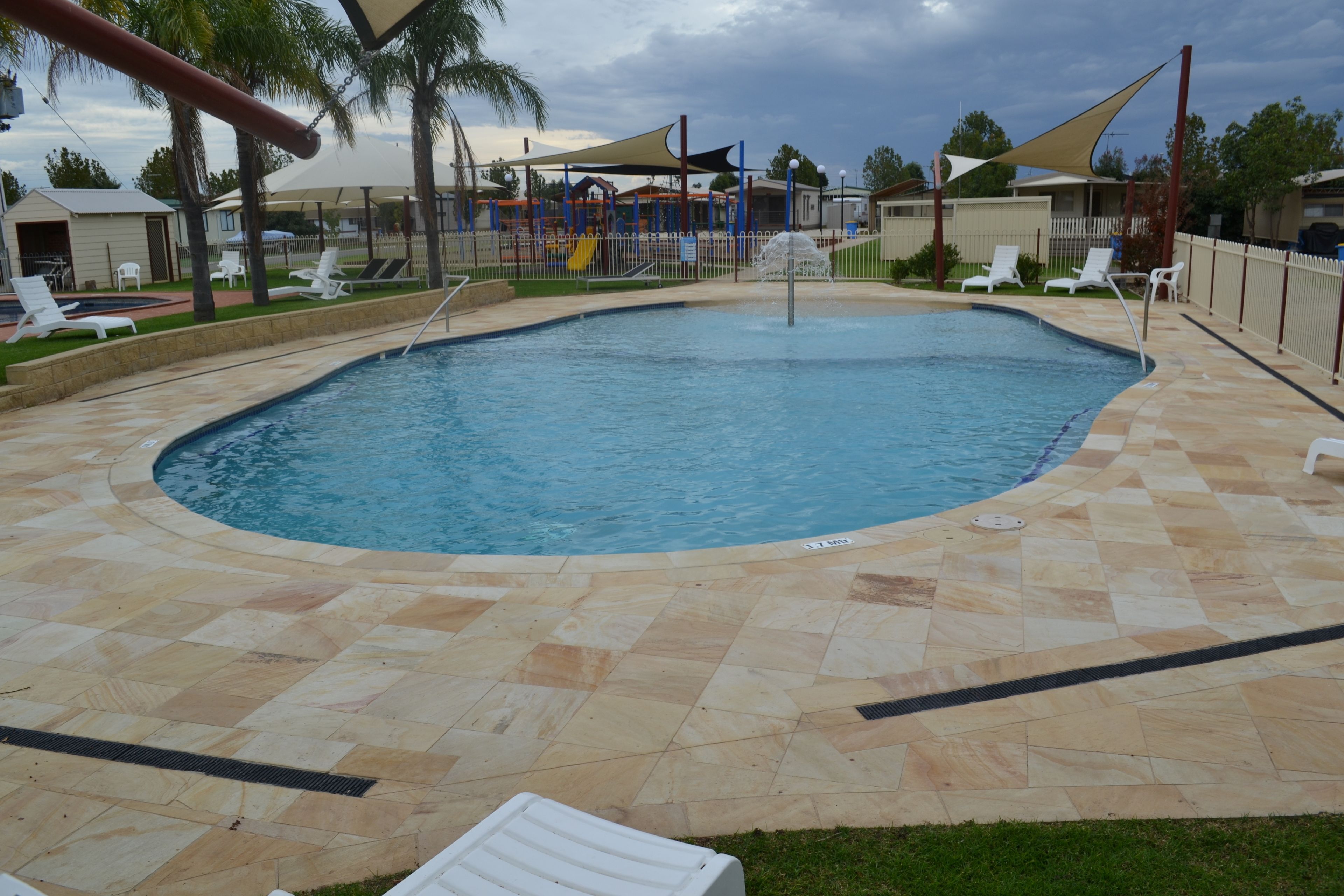 Una piscina con borde de baldosas, rodeada de sillas de descanso y palmeras.