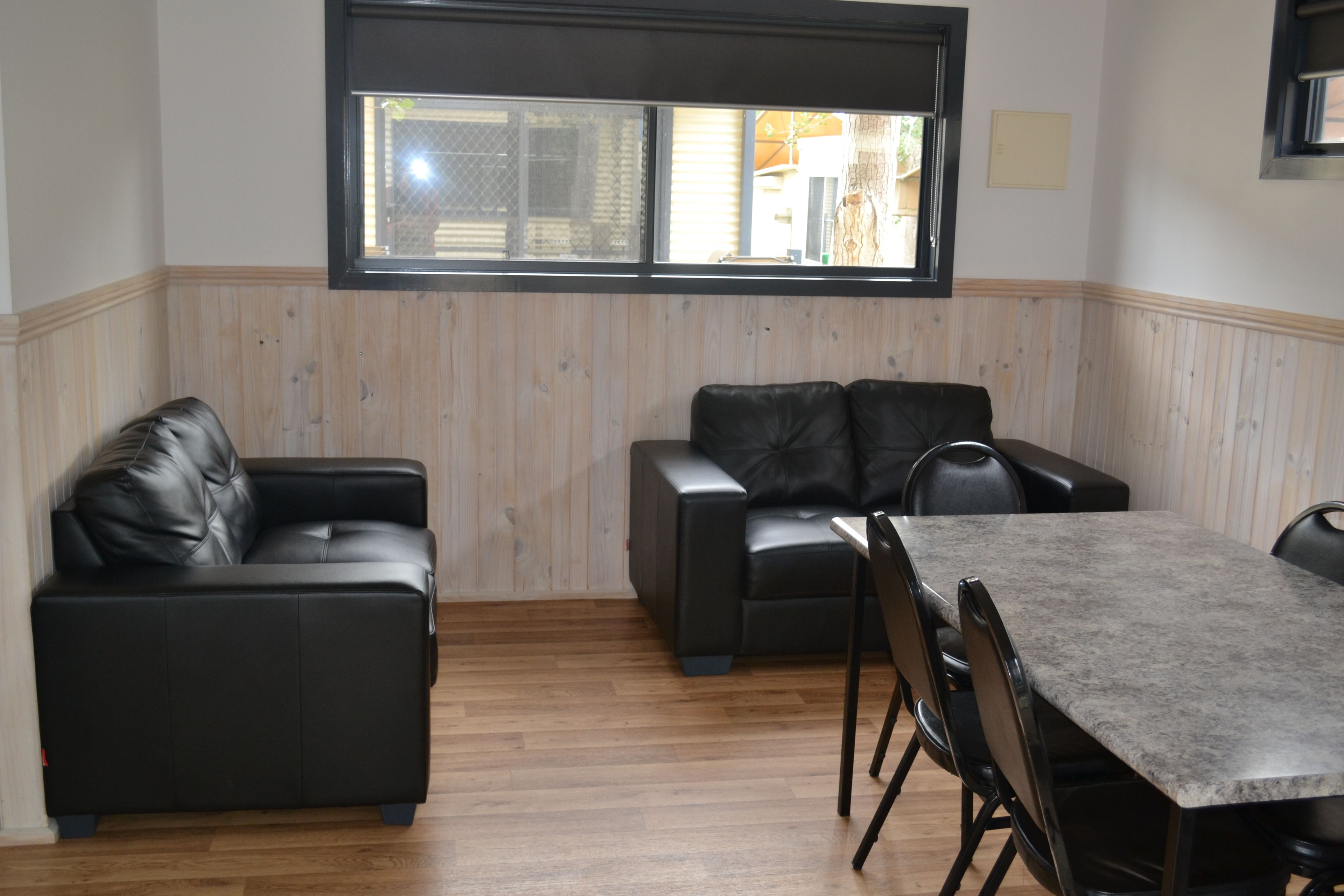 Een kamer met een houten lambrisering, een zwarte leren bank, een bijpassende fauteuil en een eettafel met stoelen.