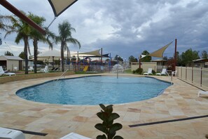 A swimming pool with a tiled deck, surrounded by lounge chairs and palm trees.