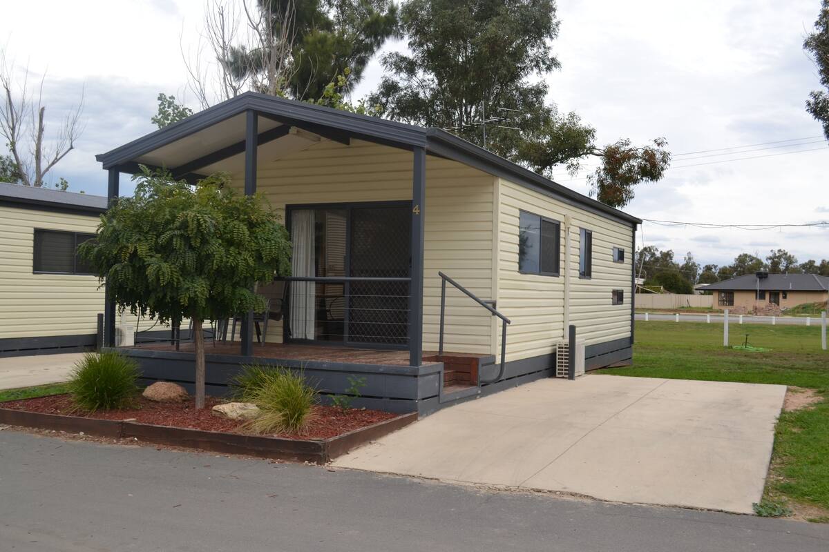 A single-story mobile home with a covered porch, a small tree, and a paved driveway.