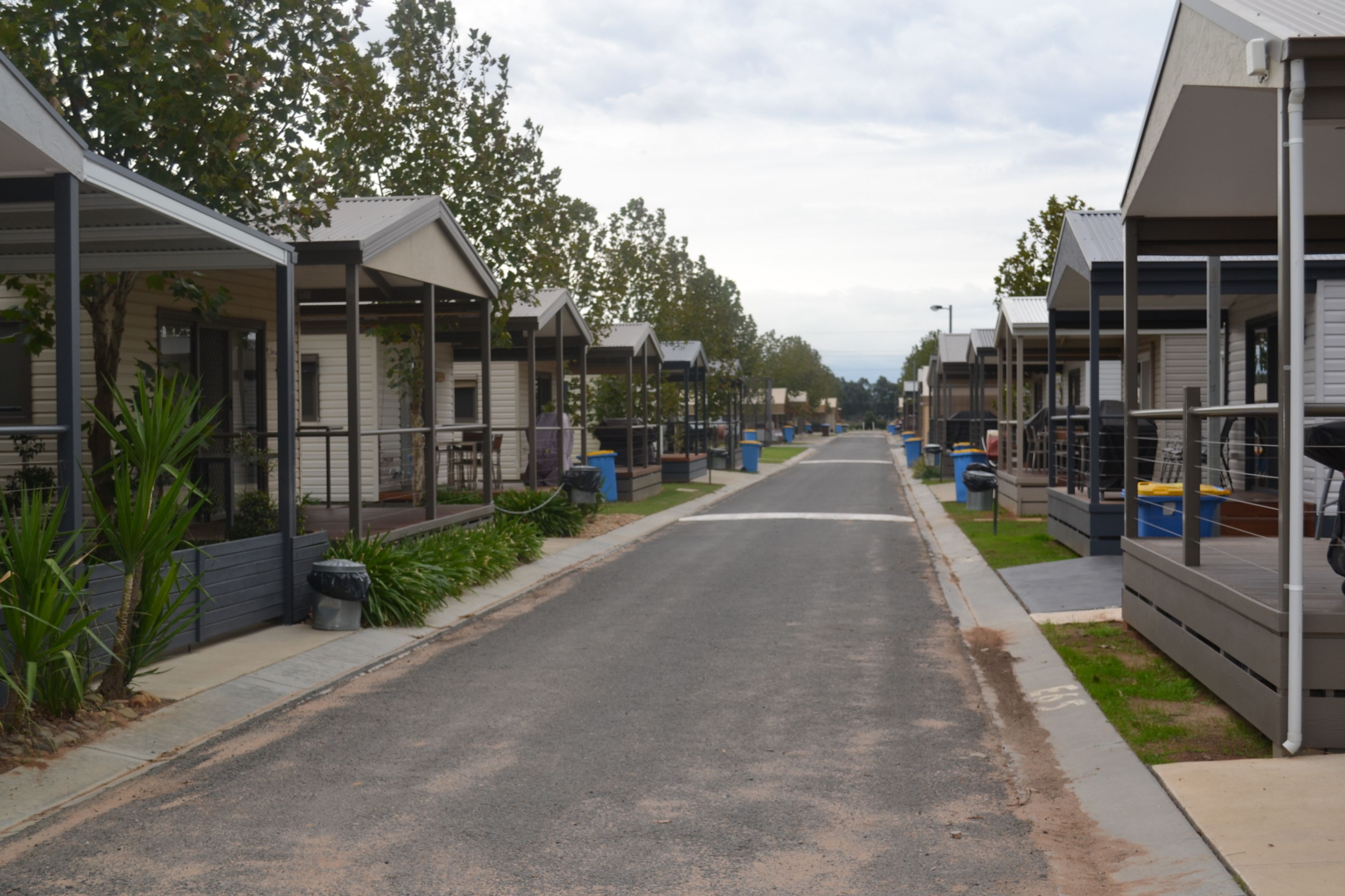 A row of modern, single-story mobile homes with covered walkways and a paved street.