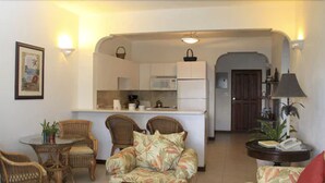 A compact living space with a kitchenette, wicker furniture, and a small dining table.