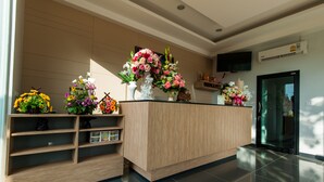 A reception desk with multiple flower arrangements, a television, and a wall-mounted air conditioning unit. - Jinda Resort (Sa Khu)