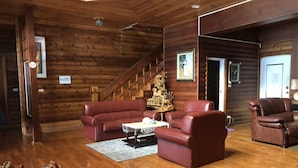 A log cabin interior with a wooden staircase, leather sofas, a coffee table, and a wooden sculpture. - Cingjing Brilliant Twins of Seattle (Ren'ai)