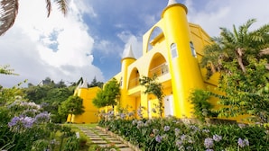 A yellow building with arched windows and a balcony, surrounded by lush greenery and purple flowers. - Cingjing Brilliant Twins of Seattle (Ren'ai)