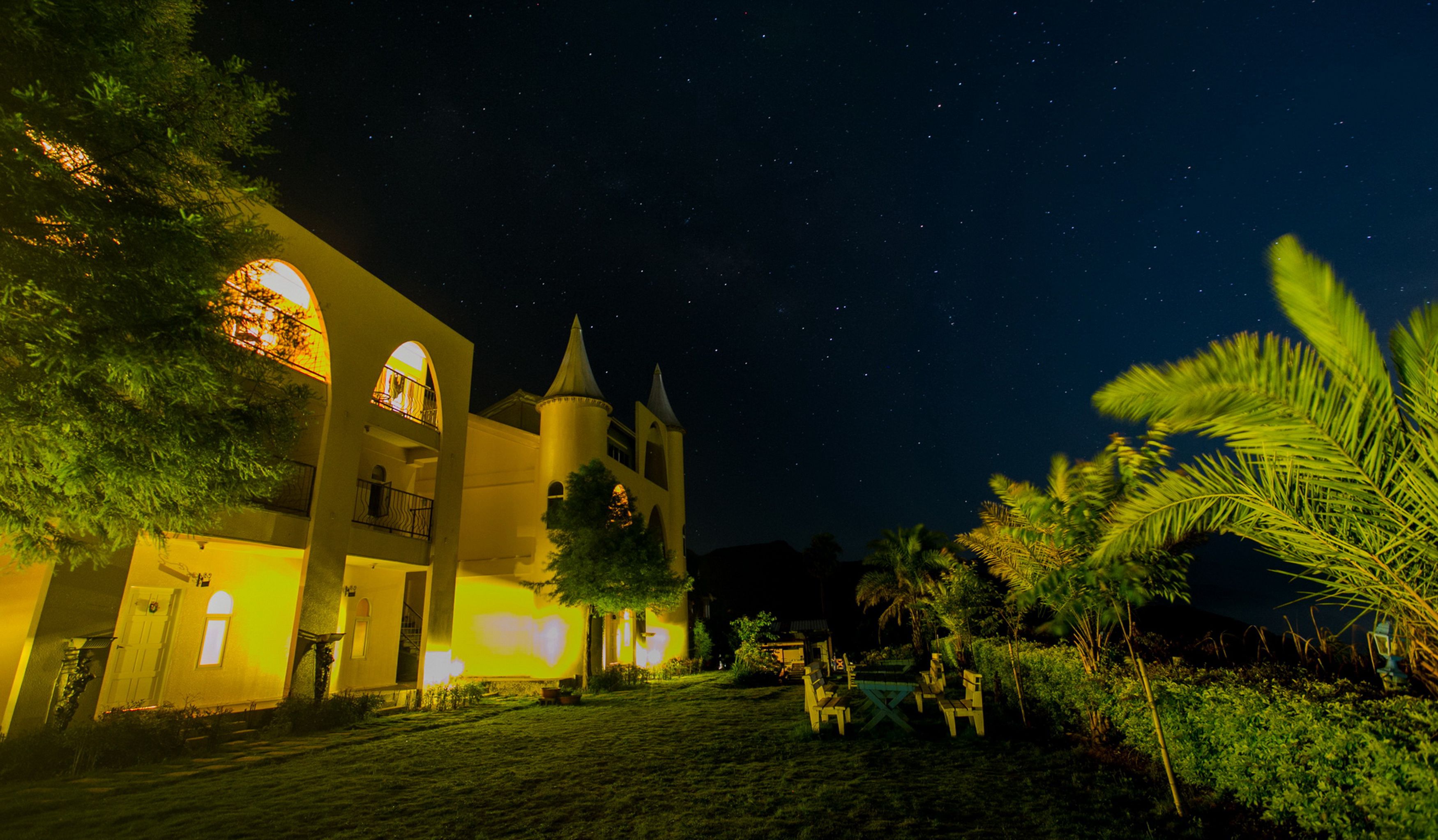A building with a tower and arched windows, surrounded by greenery and a clear night sky.