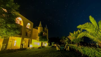 A building with a tower and arched windows, surrounded by greenery and a clear night sky.