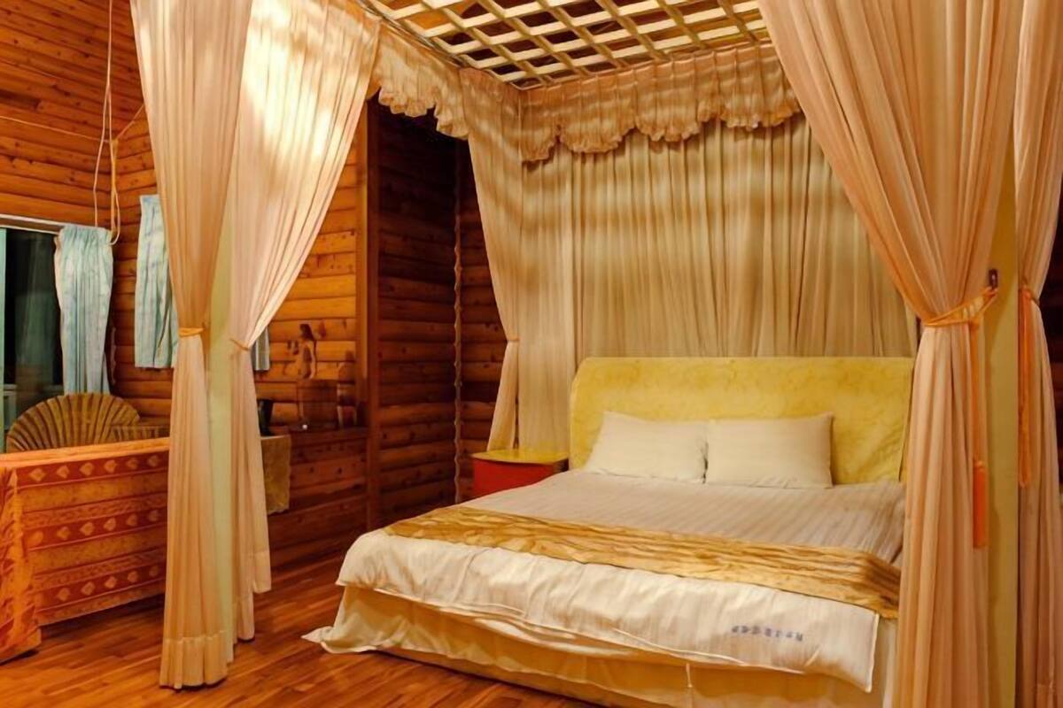 Ein Zimmer aus Holz mit einem Bett, Vorhängen und einem Ventilator.