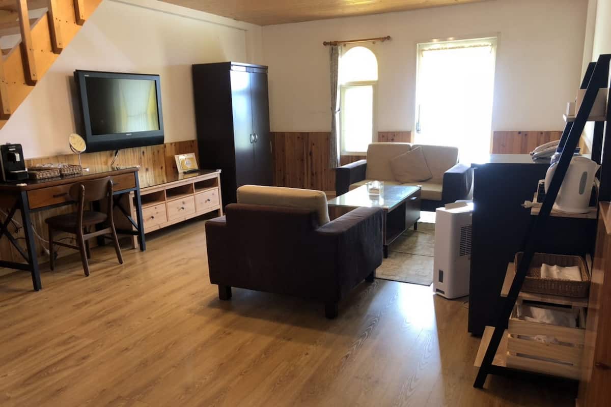 Ein Wohnzimmer mit Holzboden, einer Couch, einem Couchtisch, einem Fernseher, einem Schrank und einer Treppe.