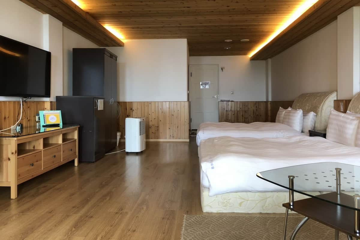 Ein modernes Hotelzimmer mit Holzboden, einem großen Bett, einem Flachbildfernseher, einem Schreibtisch und einem Kleiderschrank.