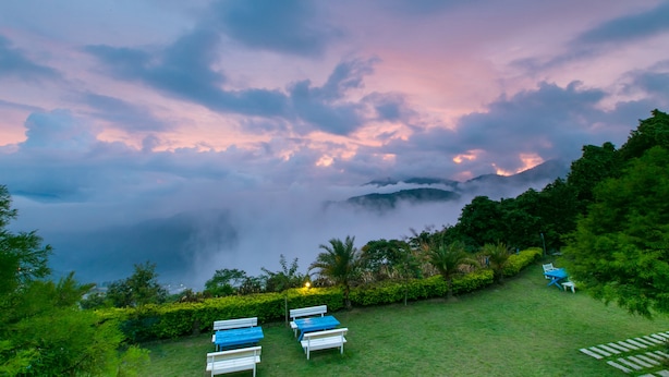 A serene outdoor seating area with benches and tables, surrounded by lush greenery and a backdrop of clouds and mountains. - Cingjing Brilliant Twins of Seattle (Ren'ai)
