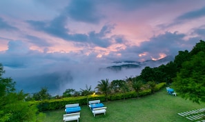 A serene outdoor seating area with benches and tables, surrounded by lush greenery and a backdrop of clouds and mountains. - Cingjing Brilliant Twins of Seattle (Ren'ai)