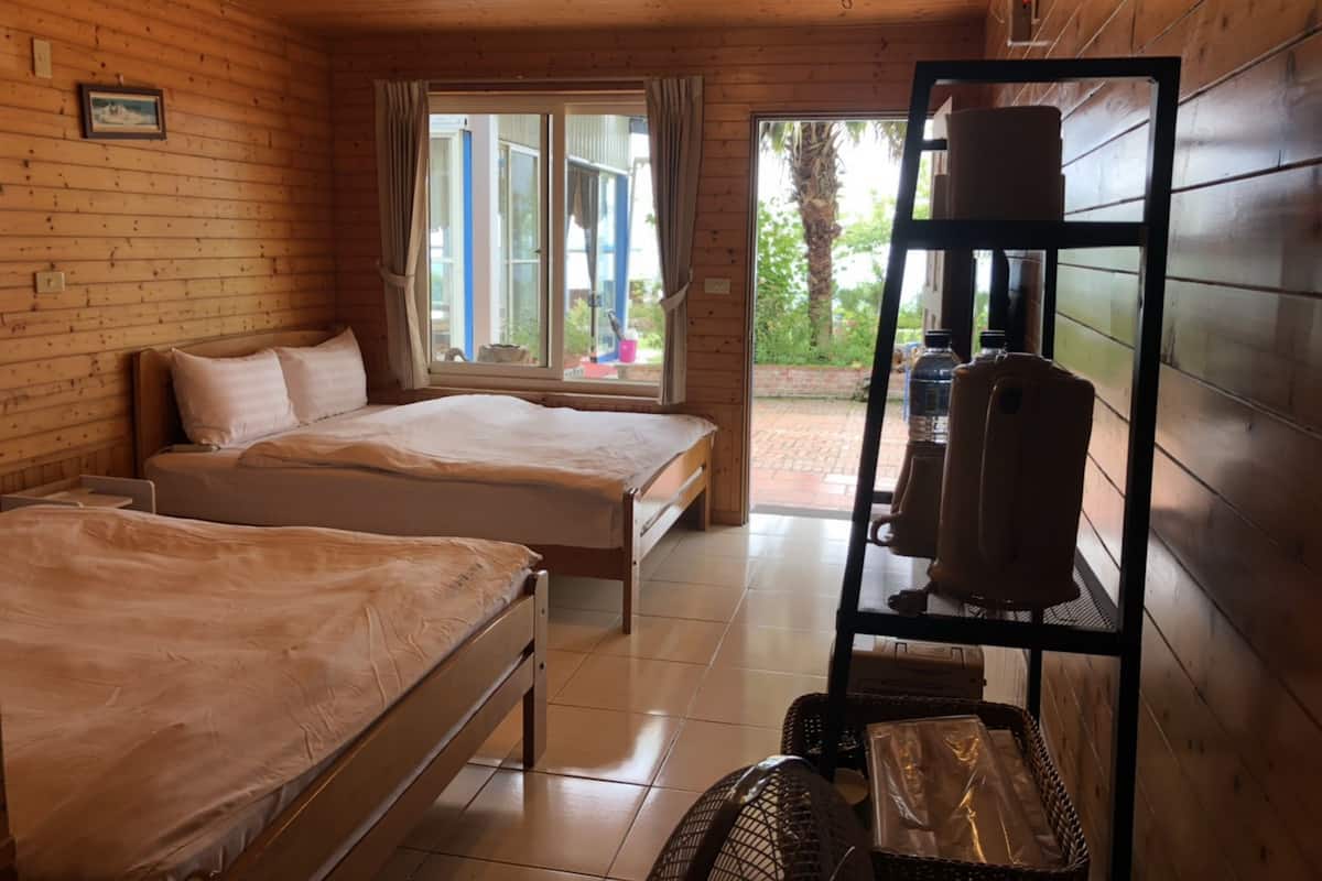 Ein Zimmer mit Holzboden und zwei Betten, einem Fenster und einem Regal mit Wasserflaschen.