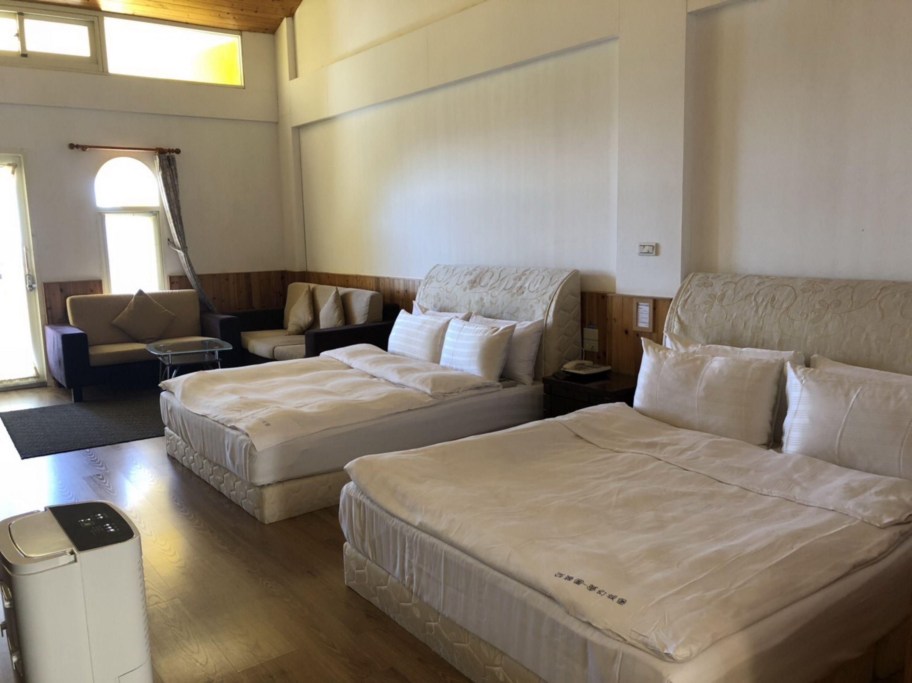Een hotelkamer met twee bedden, een bank, een eettafel en een raam met gordijnen.