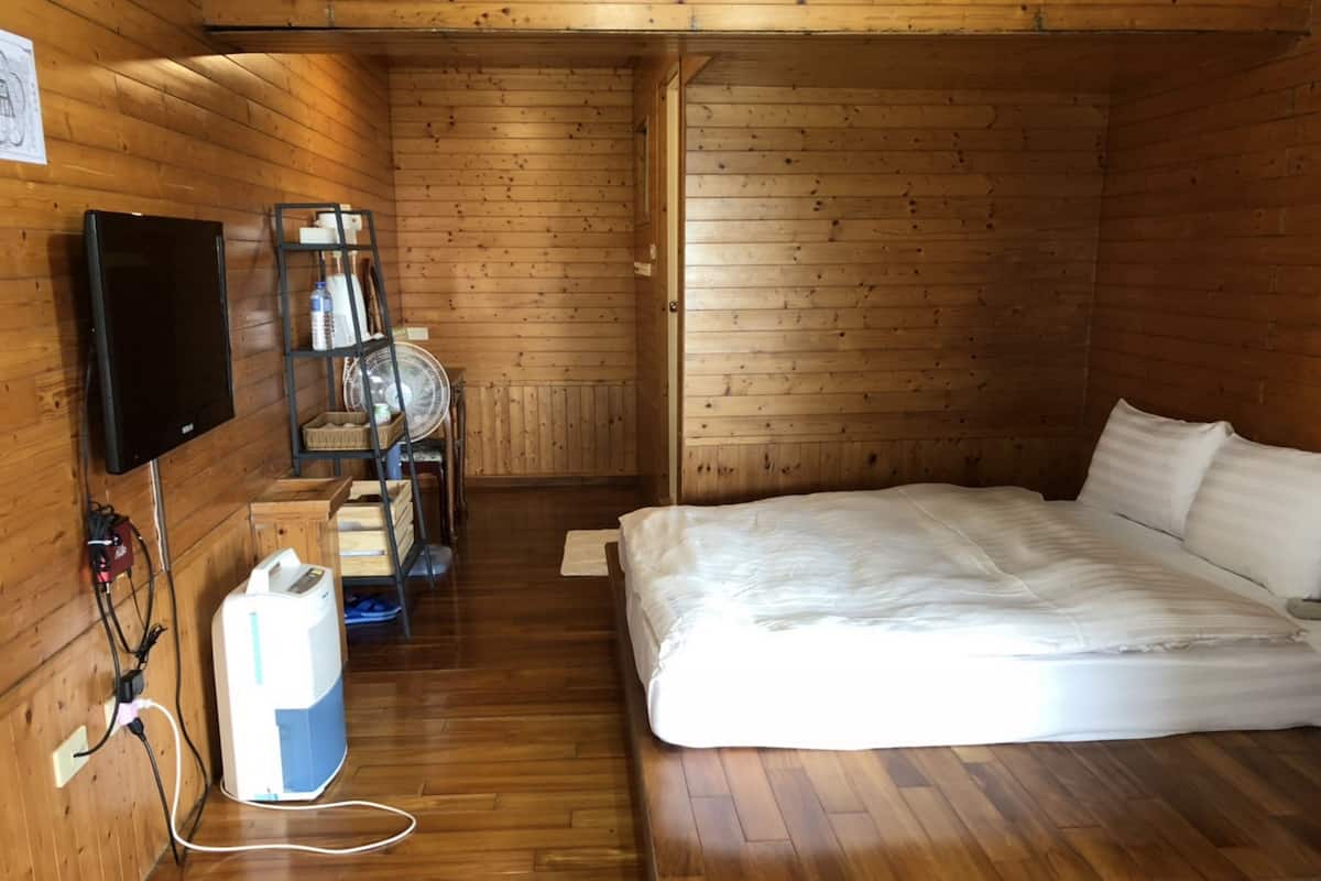 Ein Zimmer mit Holzwänden, einem Bett, einem Fernseher, einem Ventilator und einem kleinen Tisch mit einem Korb.