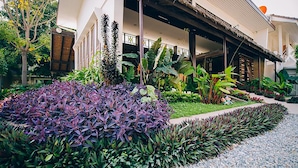 A hotel with a covered outdoor area, lush greenery, and a well-maintained garden. - Good Times Resort (Kanchanaburi)