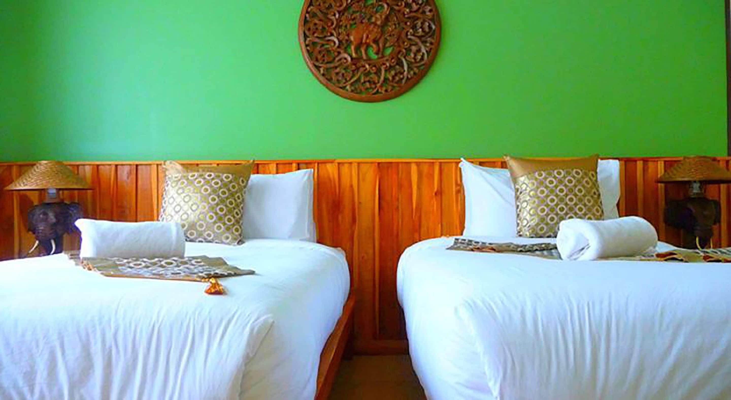 A hotel room with two beds, wooden headboards, patterned pillows, and a decorative wall hanging.
