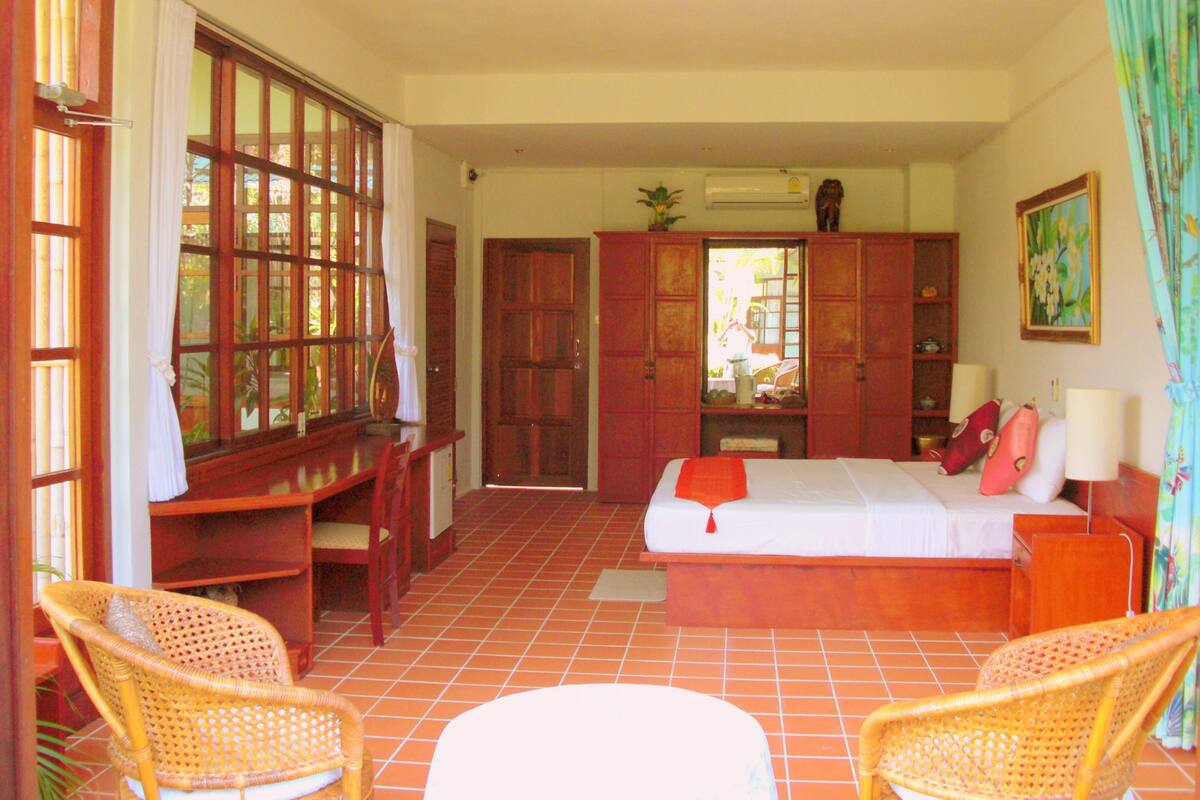 Une chambre à coucher comprenant un lit, deux fauteuils en osier, un bureau et une armoire.