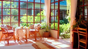 Una habitación con ventanas amplias, sillas de mimbre, una mesa y una planta en maceta.