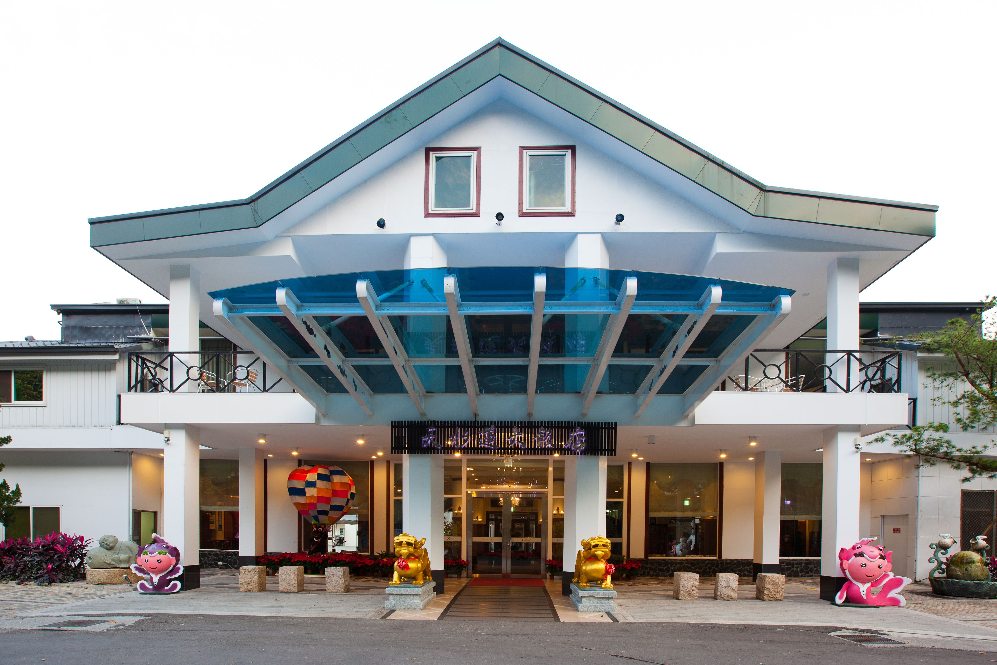 A hotel with a modern design, featuring a prominent entrance with a glass canopy and two golden lion statues at the front.
